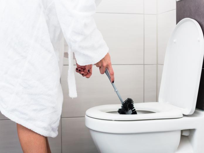 En person er ved at skrubbe et toilet med en toiletbørste. 