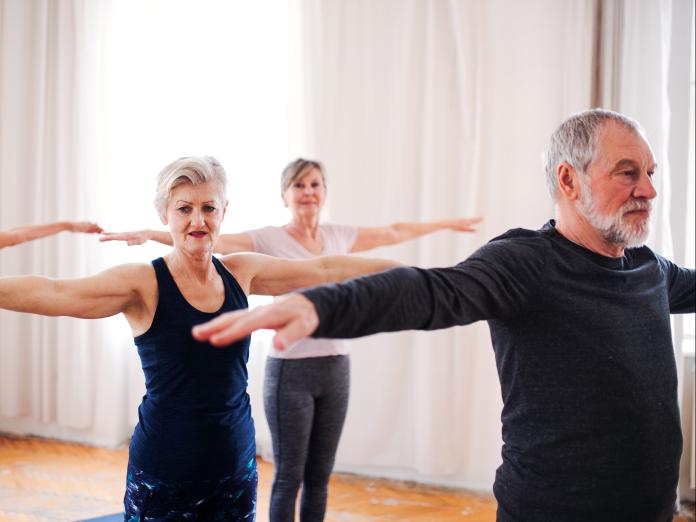 Tre ældre personer dyrker yoga og har armene strukket vandret ud.